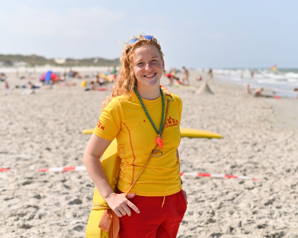 Lifeguard Demi op een zomerse dag op het strand, met badgasten op de achtergrond