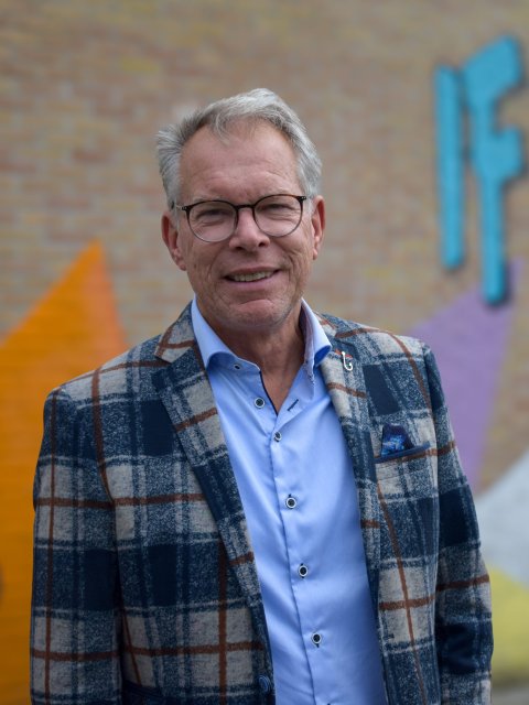Jan staat buiten voor het schoolgebouw ne kijkt in de camera