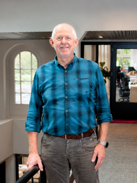 Henk staat in een gebouw en lacht in de camera