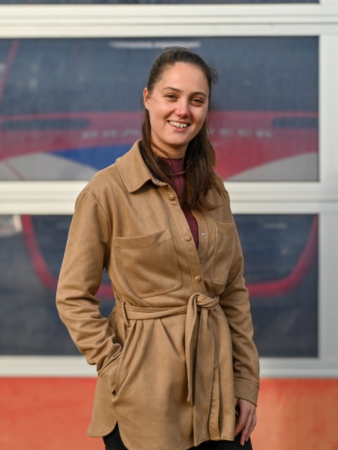 Portretfoto van Ilse voor de deuren van de brandweerkazerne, waar je een brandweerauto doorheen ziet