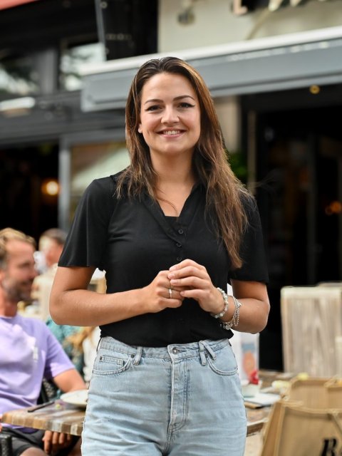 Larissa kijkt lachend in de camera terwijl ze voor het terras van 't Wapen van Terschelling staat
