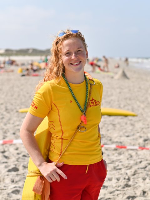 Lifeguard Demi op een zomerse dag op het strand, met badgasten op de achtergrond