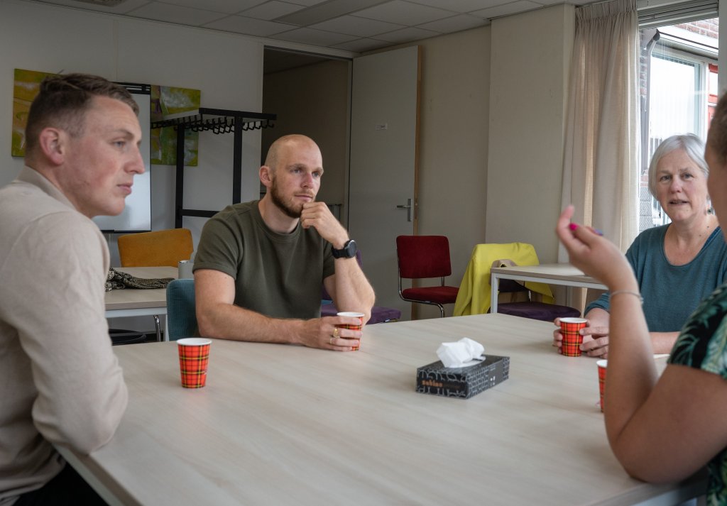 Inwoners die aan tafel met elkaar in gesprek zijn met iemand van buurtbemiddeling