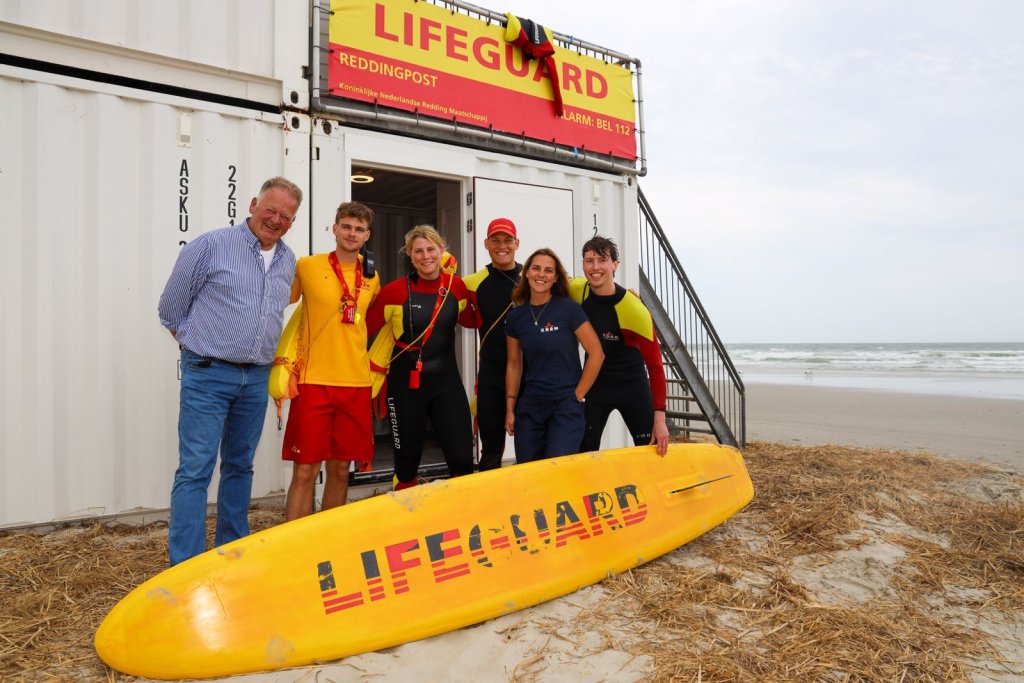 Groepsfoto van de burgemeester met vier lifeguards voor de lifeguardpost bij paal 8