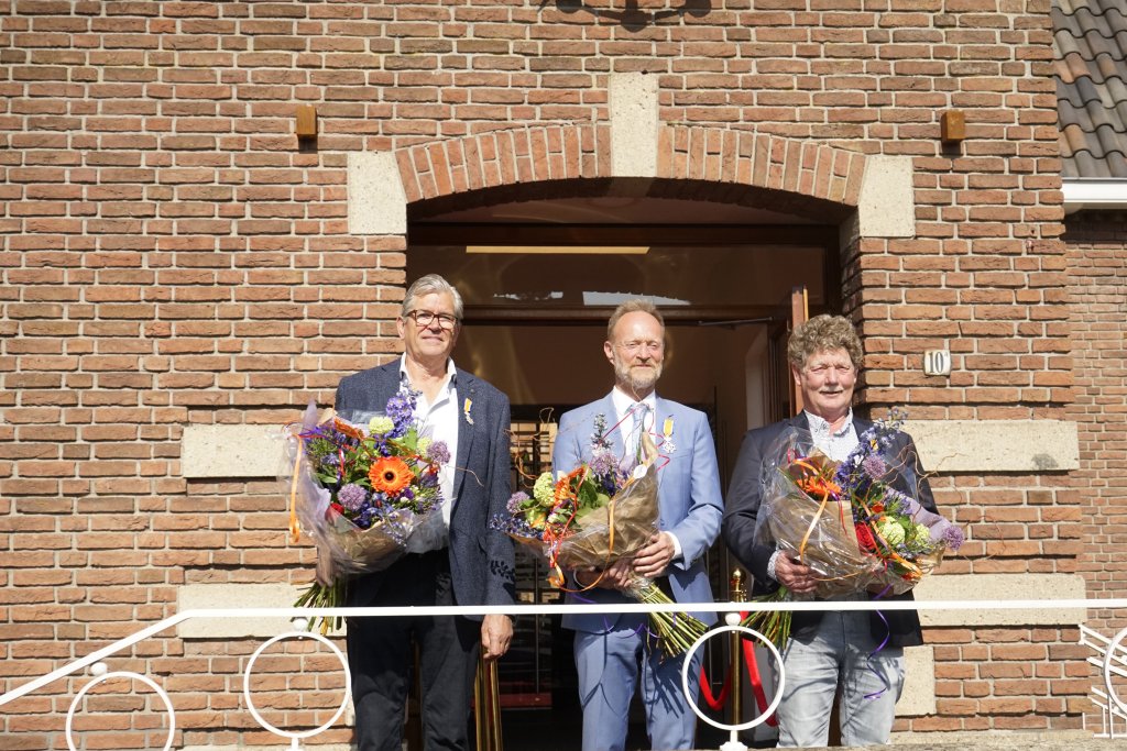 De drie gedecoreerden voor het gemeentehuis met bloemen en de lintjes