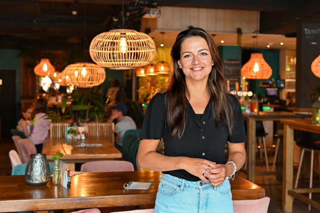 Larissa kijkt lachend in de camera terwijl ze in het restaurant staat