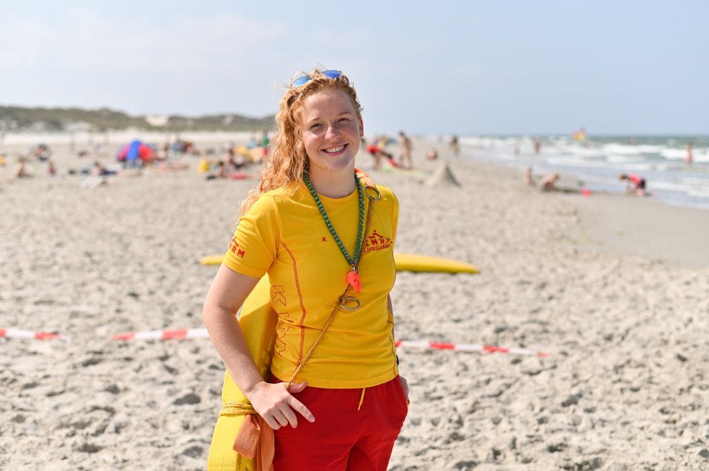 Lifeguard Demi op een zomerse dag op het strand, met badgasten op de achtergrond