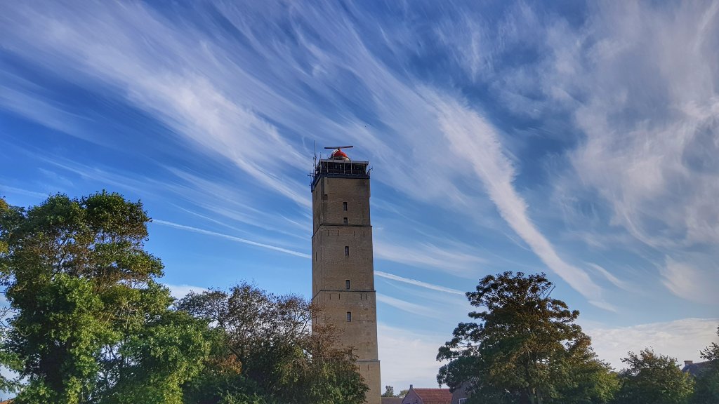 De Brandaris, de vuurtoren op West, met boomtoppen een blauwe lucht