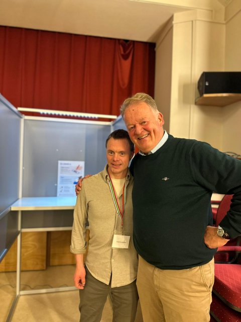 Stembureaulid Arno en burgemeester Roel Cazemier poserend voor een stemhokje.