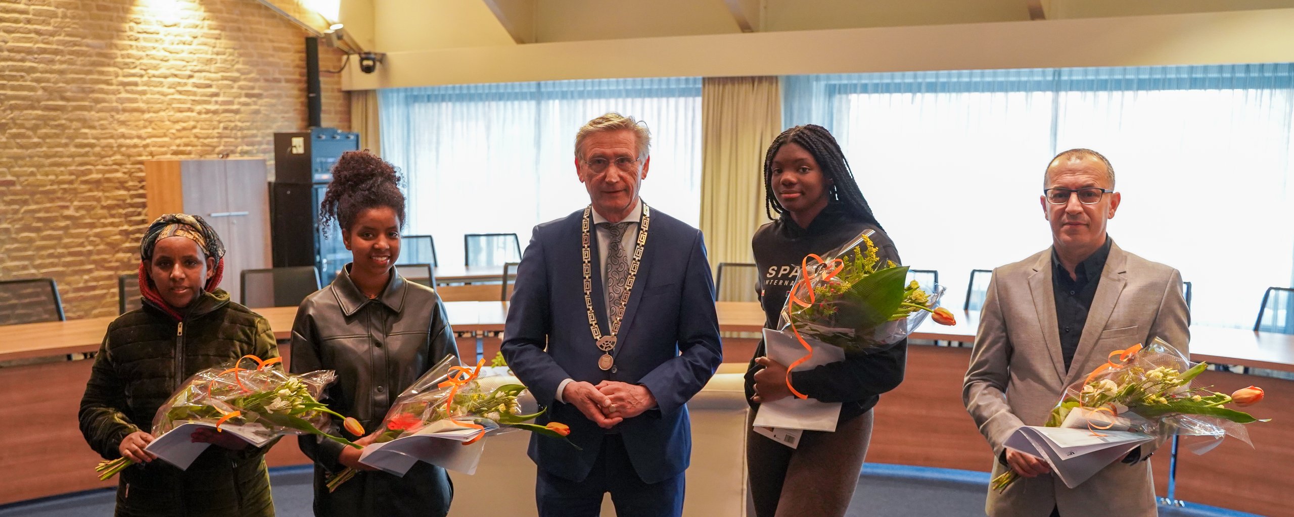 Een foto van waarnemend burgemeester Jan Westmaas met 4 nieuwe Nederlanders die hun naturalisatieceremonie hebben afgerond en nu officieel als Nederlanders worden herkent.