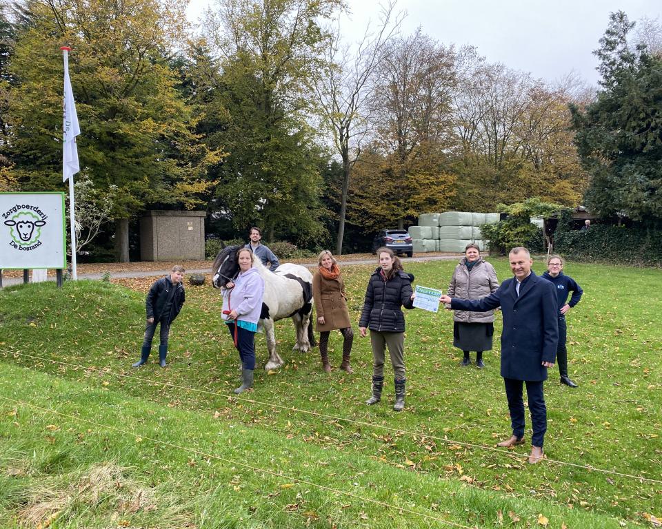 Wethouder Freek Brouwer overhandigt een cheque met een investeringssubsidie aan bewoners van zorgboerderij De Bosrand.