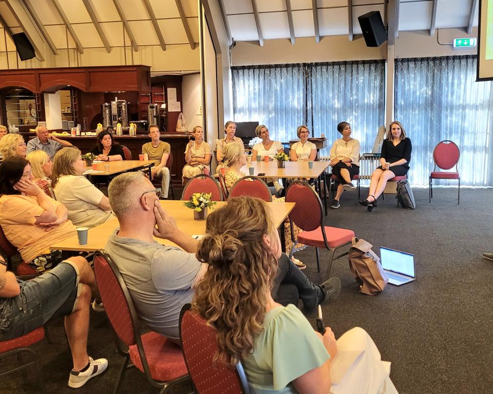 Groep vrijwiligers zit te luisteren naar wethouder Brouwer op een evaluatieavond