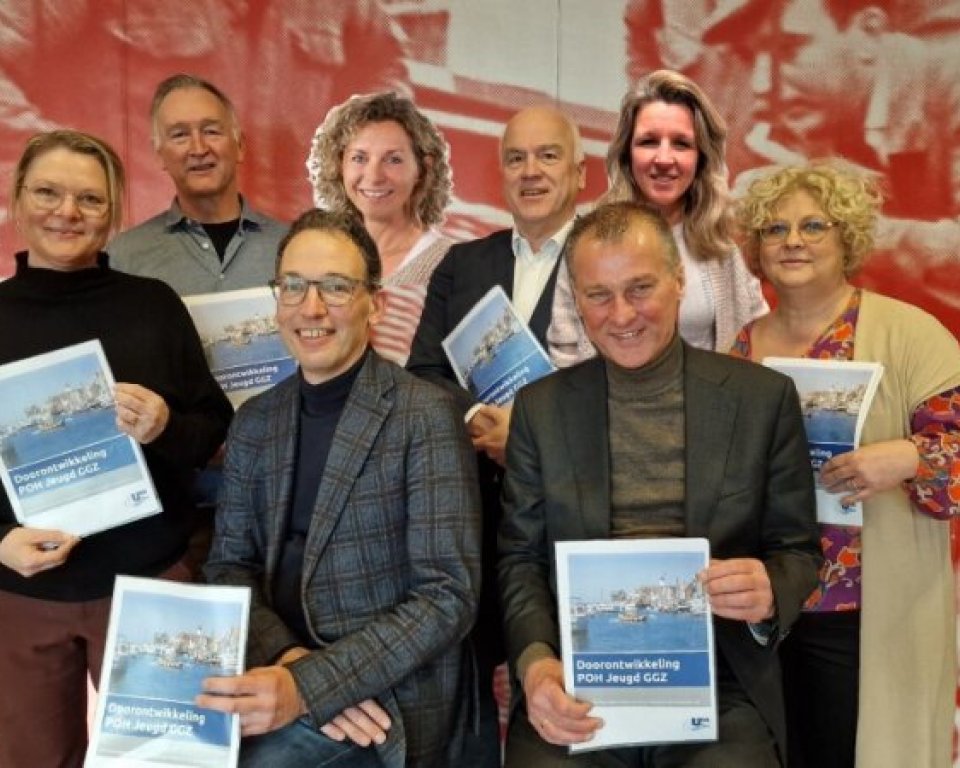 Diverse mensen met een A4 papier in de hand voor een rode achtergrond met mensen erop