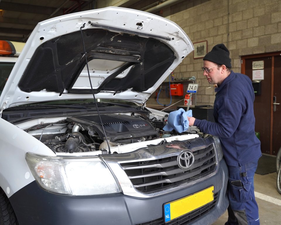 Man gekleed als monteur werkt aan auto met openstaande motorkap. 