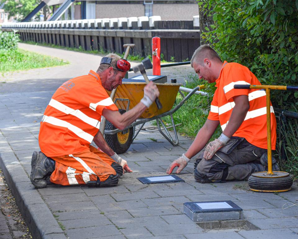 Bestratingmedewerkers leggen paalkoptegels in een stoep op Urk