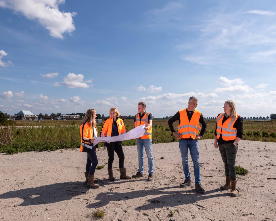 Een groep van 5 personen, 3 kijken naar een bouwtekening. De overige twee personen staan met elkaar te praten.