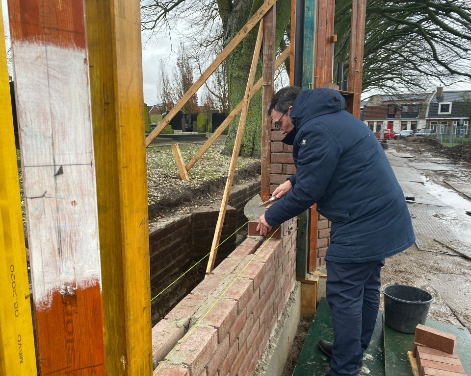 Foto van wethouder Willem Foppen die meehelpt een muur te metselen