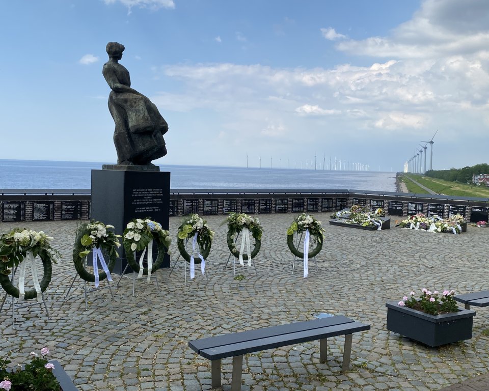 Het vissersmonument is in beeld met 5 bloemenkransen en meerdere bloemenboeketten op de achtergrond. 