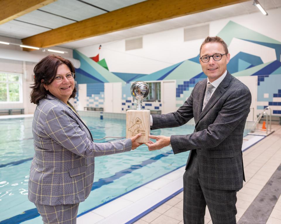 Gedeputeerde Cora Smelik van Provincie Flevoland overhandigt aan Urker wethouder Gerrit Post jr. een symbolisch cadeau als aftrap van het Ontzorgingsprogramma Verduurzaming Klein Maatschappelijk Vastgoed. 