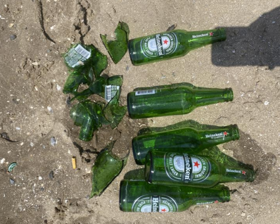 Groene Heineken bierflesje in het zand, links liggen kapotte flesjes