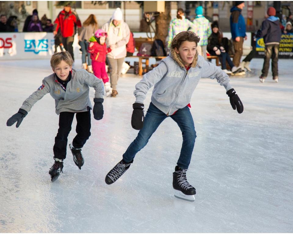 Twee jongens met een grijze jas schaatsen op een kunstbaan