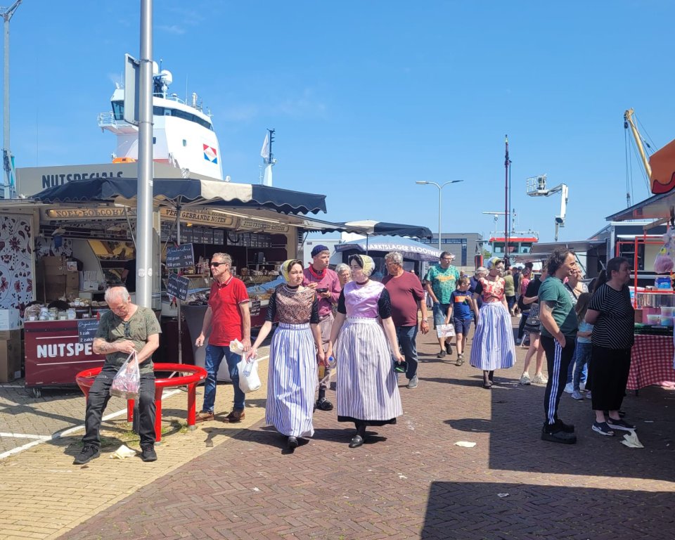 Een foto van de zaterdagmarkt van 2023 in de foto zijn twee kramen te zien met meerdere mensen gekleed in Urker klederdracht 