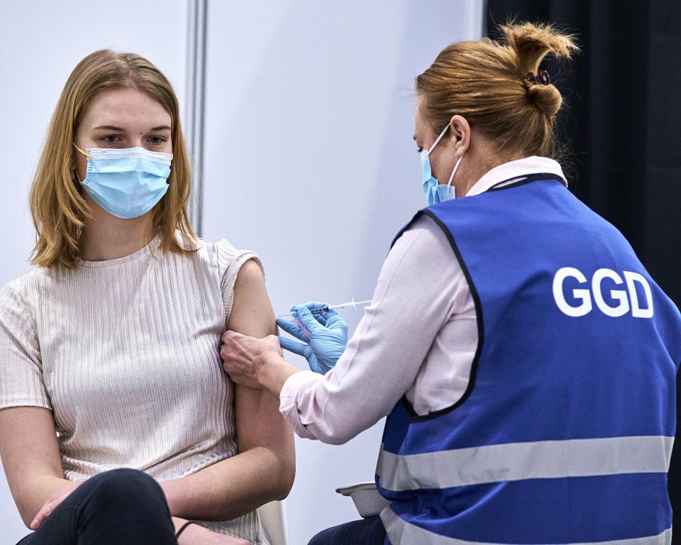 Een jonge vrouw krijg een vaccinatie in haar linkerarm van een GGD-medewerker