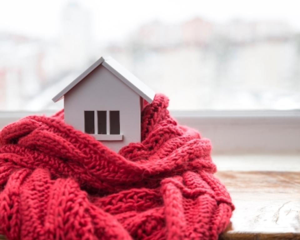 Een klein wit houten huisje op een vensterbank met een roze sjaal er om heen.