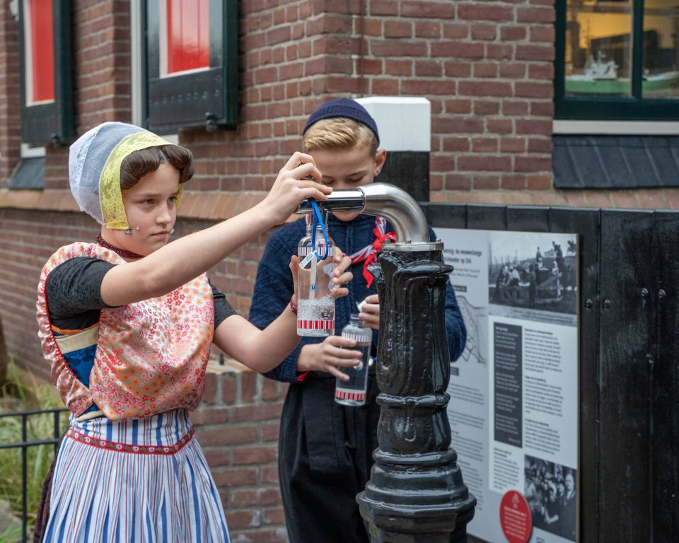 Kinderen in Urker klederdracht tappen water
