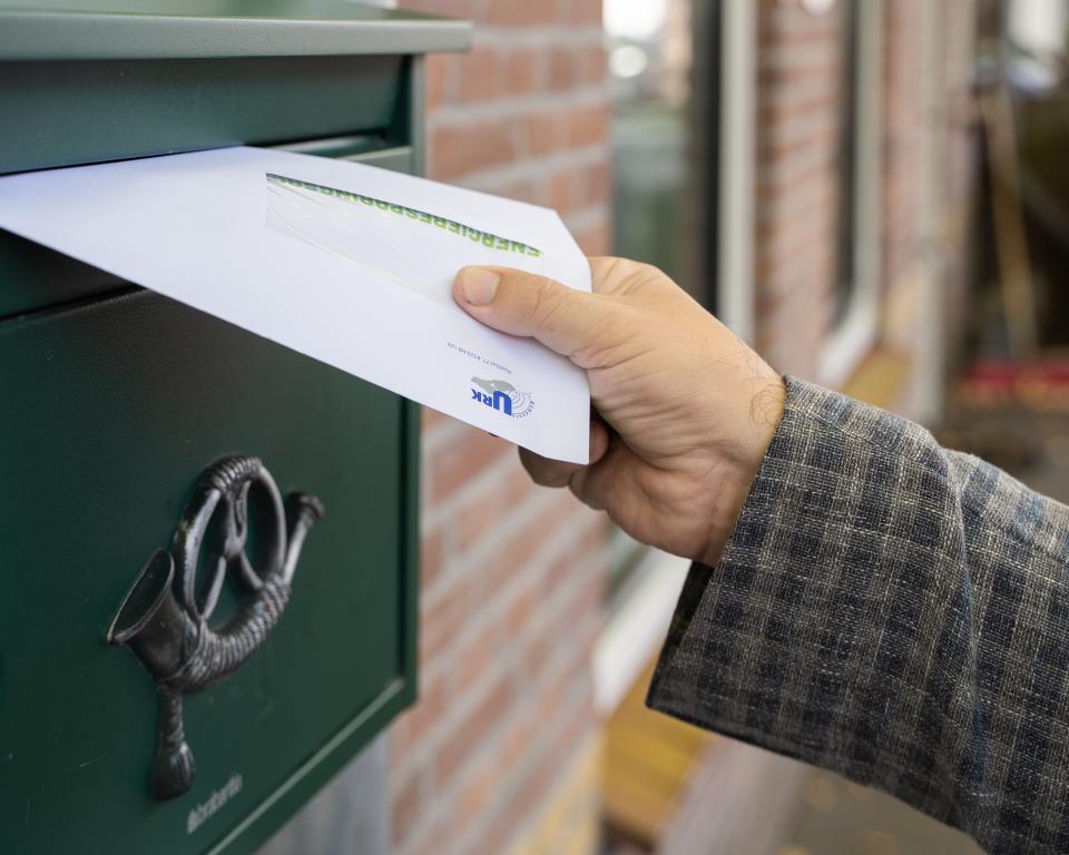 Er wordt een witte envelop in een groene muurbrievenbus gedaan