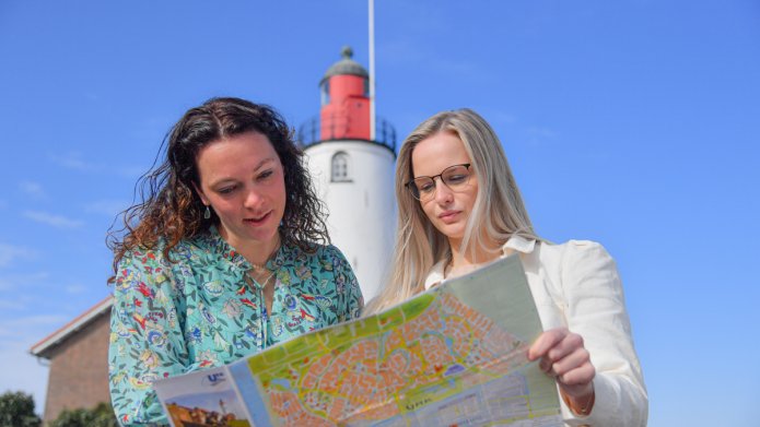 Twee vrouwen kijken op een kaart en staan voor een vuurtoren