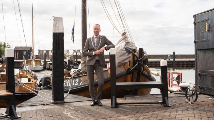 Burgemeester Cees van den Bos staat voor een houten schip met de naam UK 12 in de haven van Urk