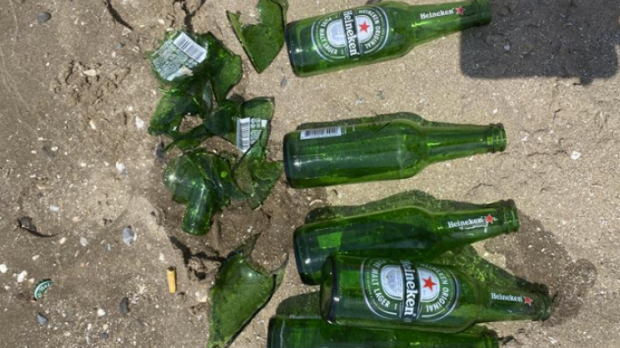 Groene Heineken bierflesje in het zand, links liggen kapotte flesjes