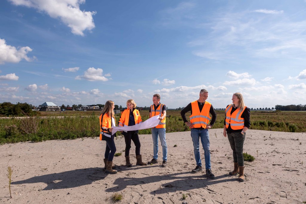 Een groep van 5 personen, 3 kijken naar een bouwtekening. De overige twee personen staan met elkaar te praten.