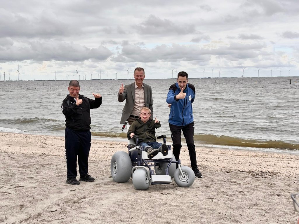 Op de foto ziet u de nieuwe strandrolstoel met van links naar rechts: Ali Pernacie, wethouder Freek Brouwer, in de rolstoelstrandstoel Rinze Kramer en Johan Blom. 