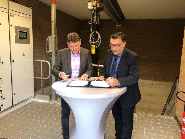 Heemraad Jo Caris en wethouder Willem Foppen staan achter een witte statafel en ondertekenen het afvalwaterakkoord