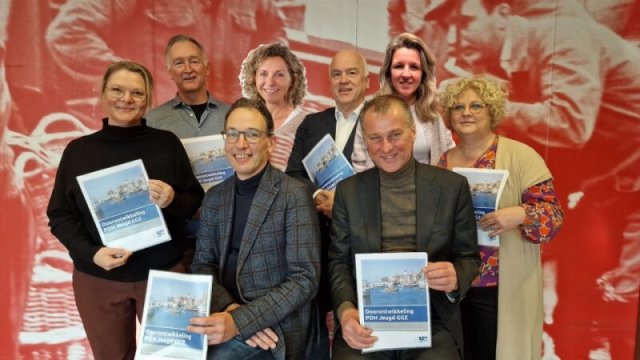 Diverse mensen met een A4 papier in de hand voor een rode achtergrond met mensen erop