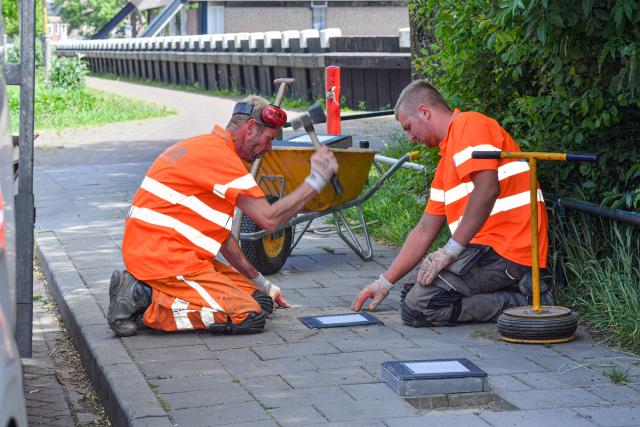 Bestratingmedewerkers leggen paalkoptegels in een stoep op Urk