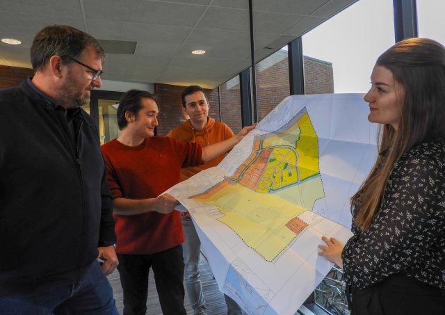 Drie mannen en een vrouw houden een tekening vast van een plattegrond