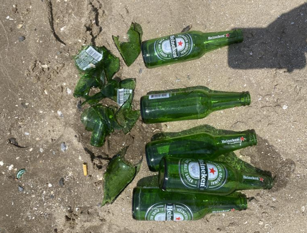 Groene Heineken bierflesje in het zand, links liggen kapotte flesjes