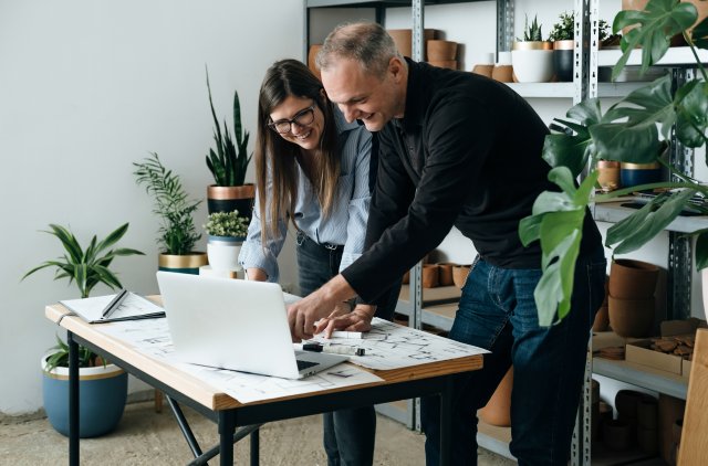 Man en vrouw staan bij een laptop met bouwtekeningen