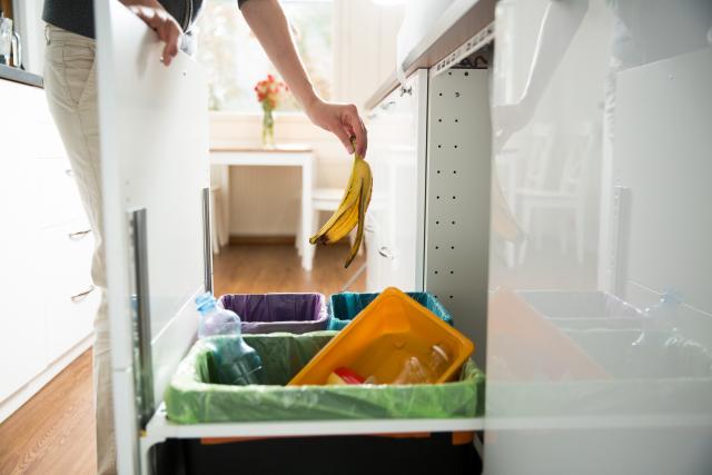 Persoon in een witte keuken gooit een bananenschil in een afvalbak