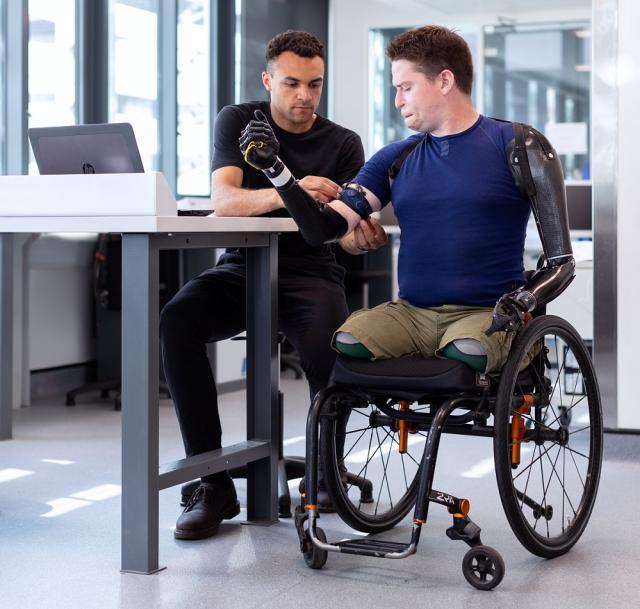 Afbeelding van man in rolstoel met een armprothese en een man achter een bureau