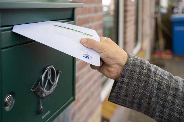 Er wordt een witte envelop in een groene muurbrievenbus gedaan