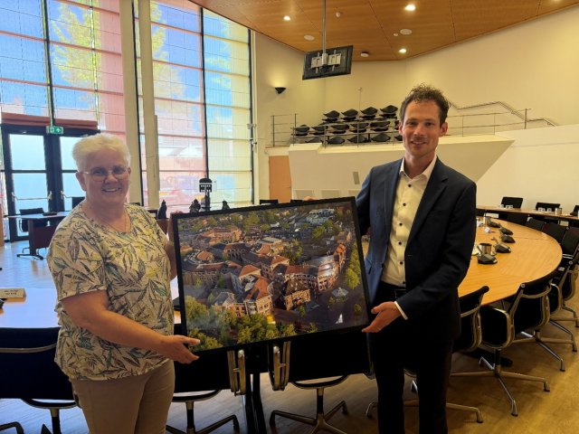 Foto van de winnaar van de wedstrijd en de wethouder met een fotolijst met de winnende foto