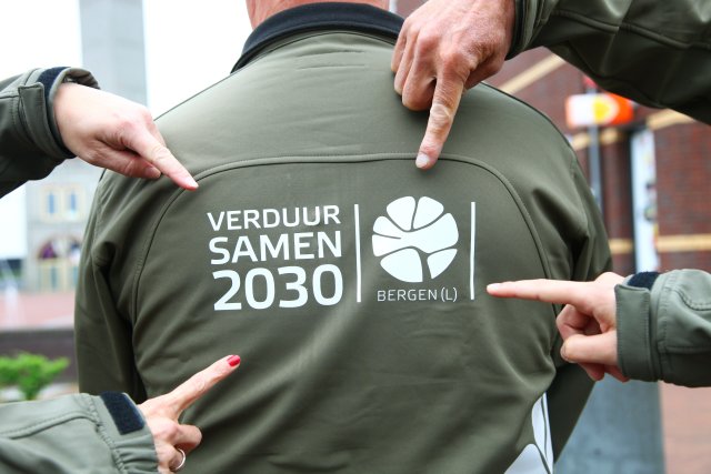 Vier handen wijzen naar het VerduurSAMEN2030 logo op de achterkant van een jas