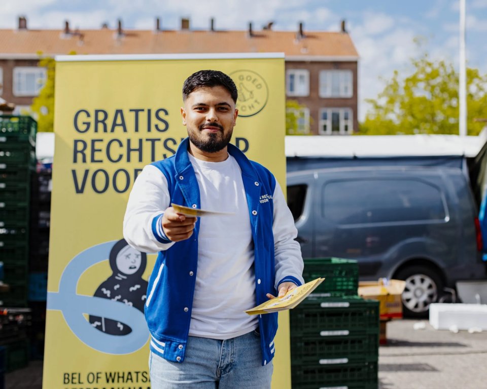 A young man holds up a flyer from Je Goed Recht; in the background is a banner that reads "Free legal aid for you."