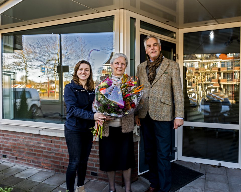 wethouder van Orselen met wooncoach op bezoek bij mevr de bruin en overhandigd een bos bloemen.