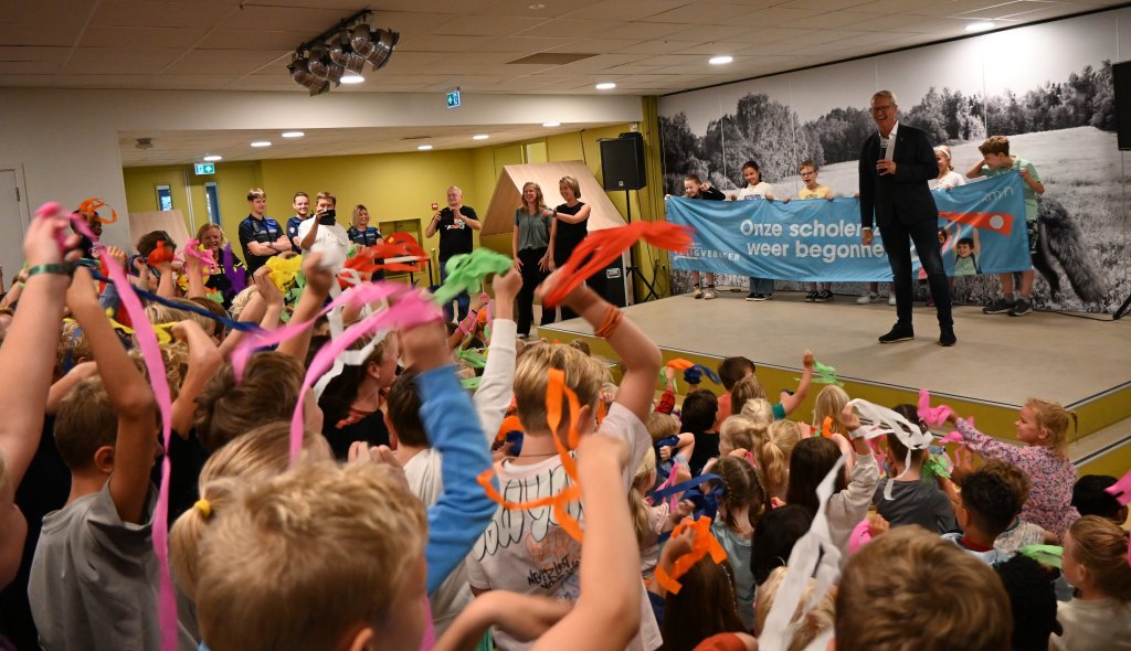 De wethouder kijkt lachend hoe de leerlingen met linten zwaaien