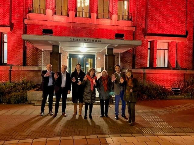 De burgemeester en wethouders van Voorschoten staan samen met de leden van de Soroptimistclub Wassenaar/Voorschoten voor het oranje gekleurde gemeentehuis.